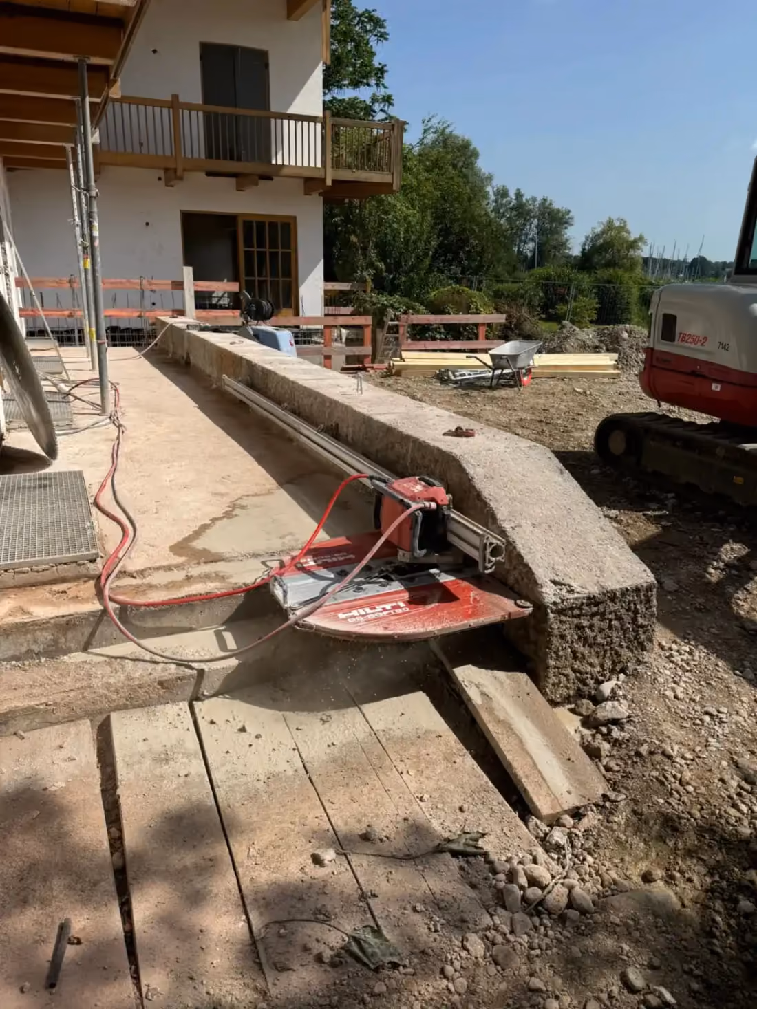Betonsäge auf einer Führungsschiene schneidet an einem Betonsockel neben einem Wohnhaus