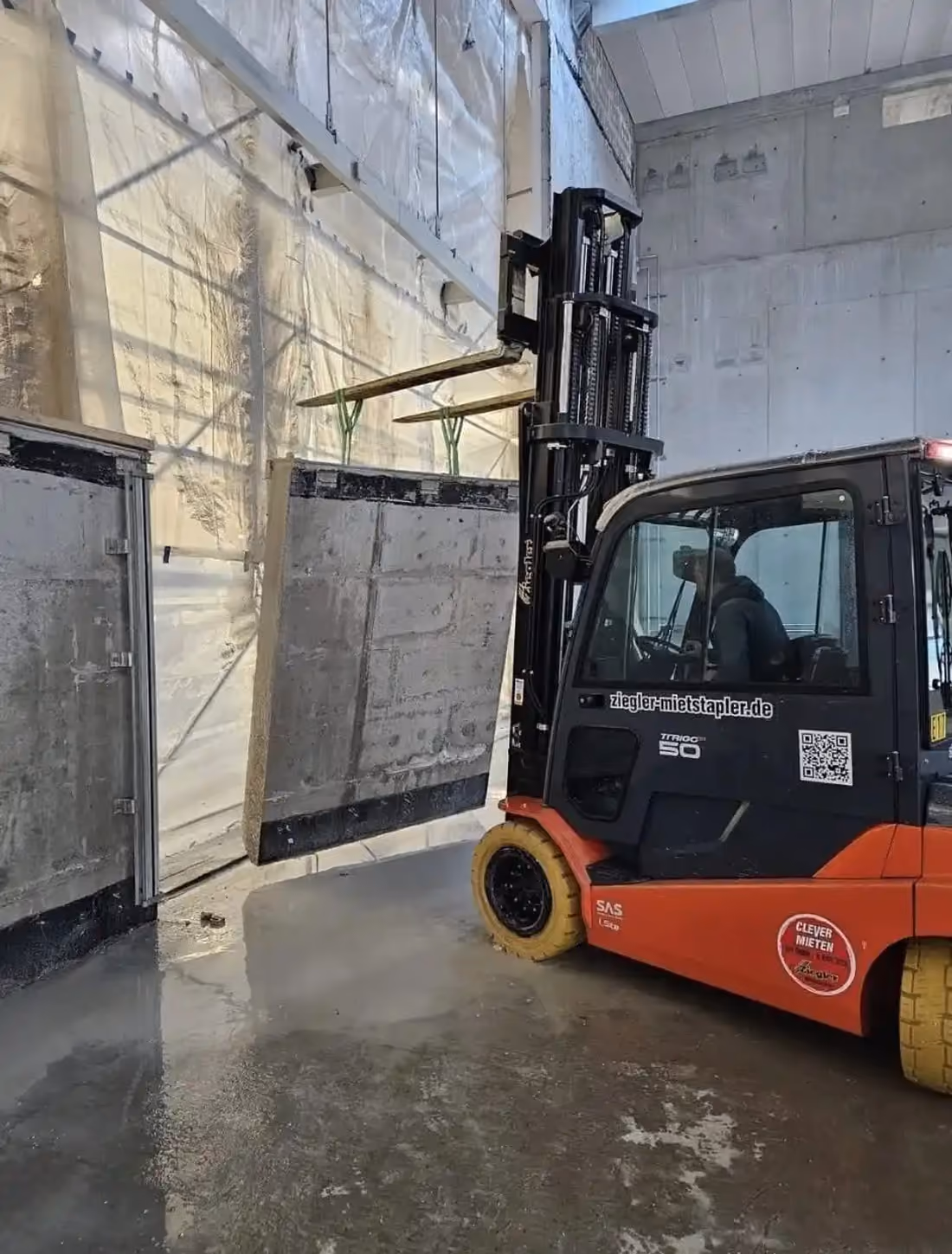 Roter Gabelstapler transportiert eine Betonplatte in einer Halle