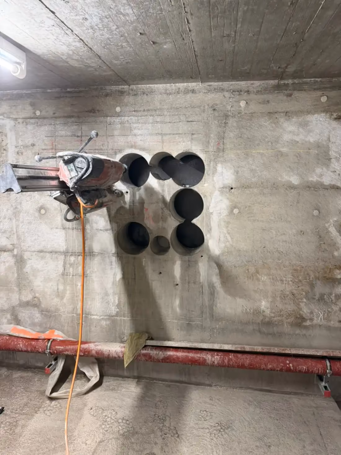 Mehrere runde Kernbohrungen in einer Betonwand, links die Kernbohrmaschine
